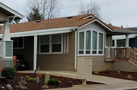 Tan Manufactured home with a nice bay window. The home is located in in a manufactured home community.
